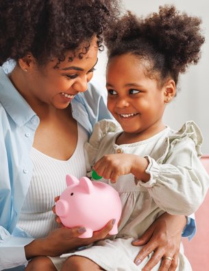 An African American mother help her daughter put money in a piggy bank.