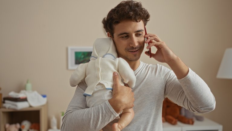Father speaking on the phone while holding a newborn baby.