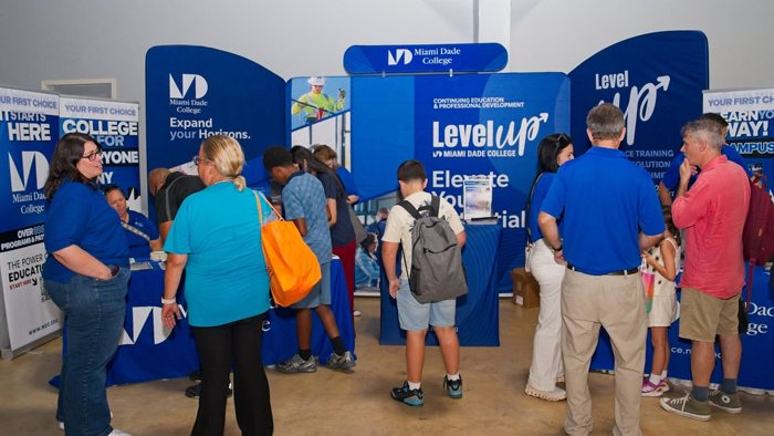 Several adults and youth standing in front of a college booth in an expo setting.