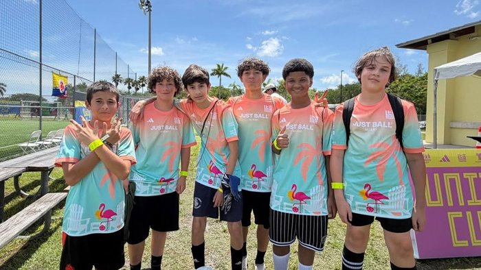 A group of boys standing in a row side-by-side, posing for the photo in soccer uniforms.